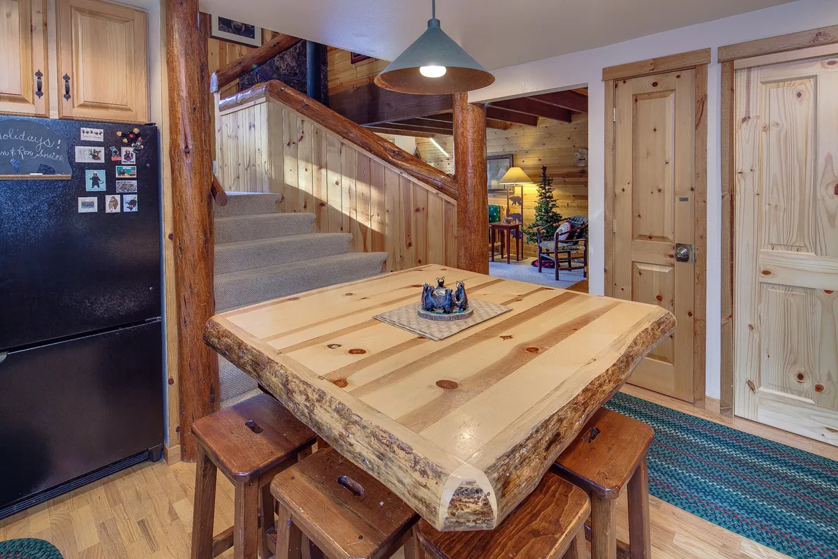 A dining area with a rustic wooden table set for a family meal, adjacent to a staircase and complemented by warm wooden tones and decorative accents. It evokes the sense of gathering and shared feasts central to the lodge experience.