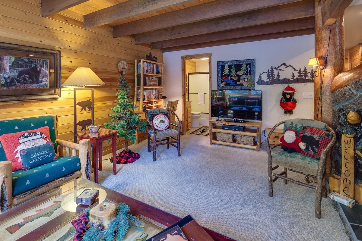 This image showcases a cozy living area featuring rustic wooden beams across the ceiling, a festive decorative tree, and a comfortable seating arrangement centered around a rustic coffee table. The warm lighting and inviting setup make it the perfect spot for movie nights or quiet relaxation after a day of adventure.