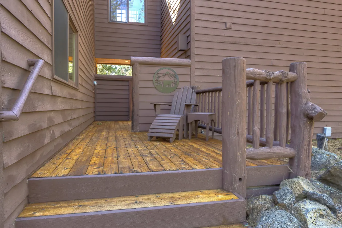 A tranquil wooden deck with adirondack chairs and rustic log railings, set against the backdrop of serene forest. The space invites conversation, relaxation, and taking in the peaceful environment, especially as the sun sets or the stars emerge.