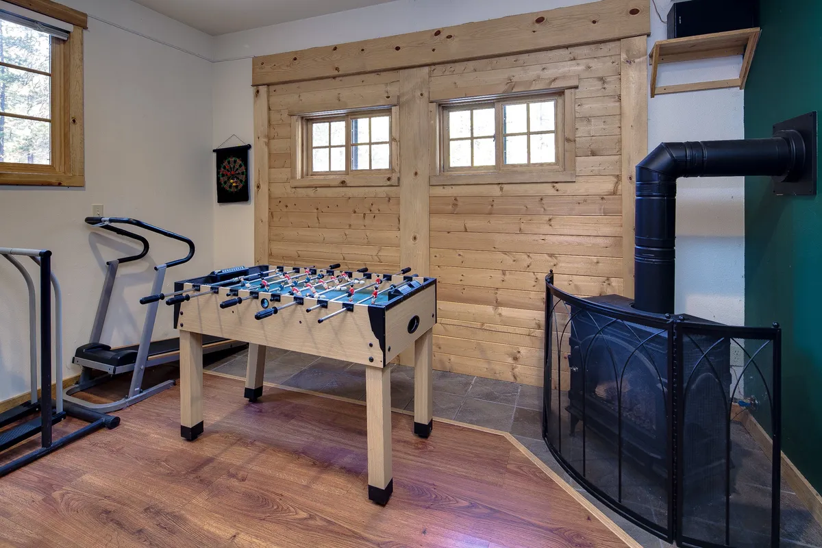 This image features a foosball table as the central focus, complemented by additional amenities like exercise equipment, a fireplace, and wood-paneled walls. The scene exudes a lively, casual energy ideal for social gatherings and game nights, and the presence of the foosball table directly connects to the section's description of the game room.