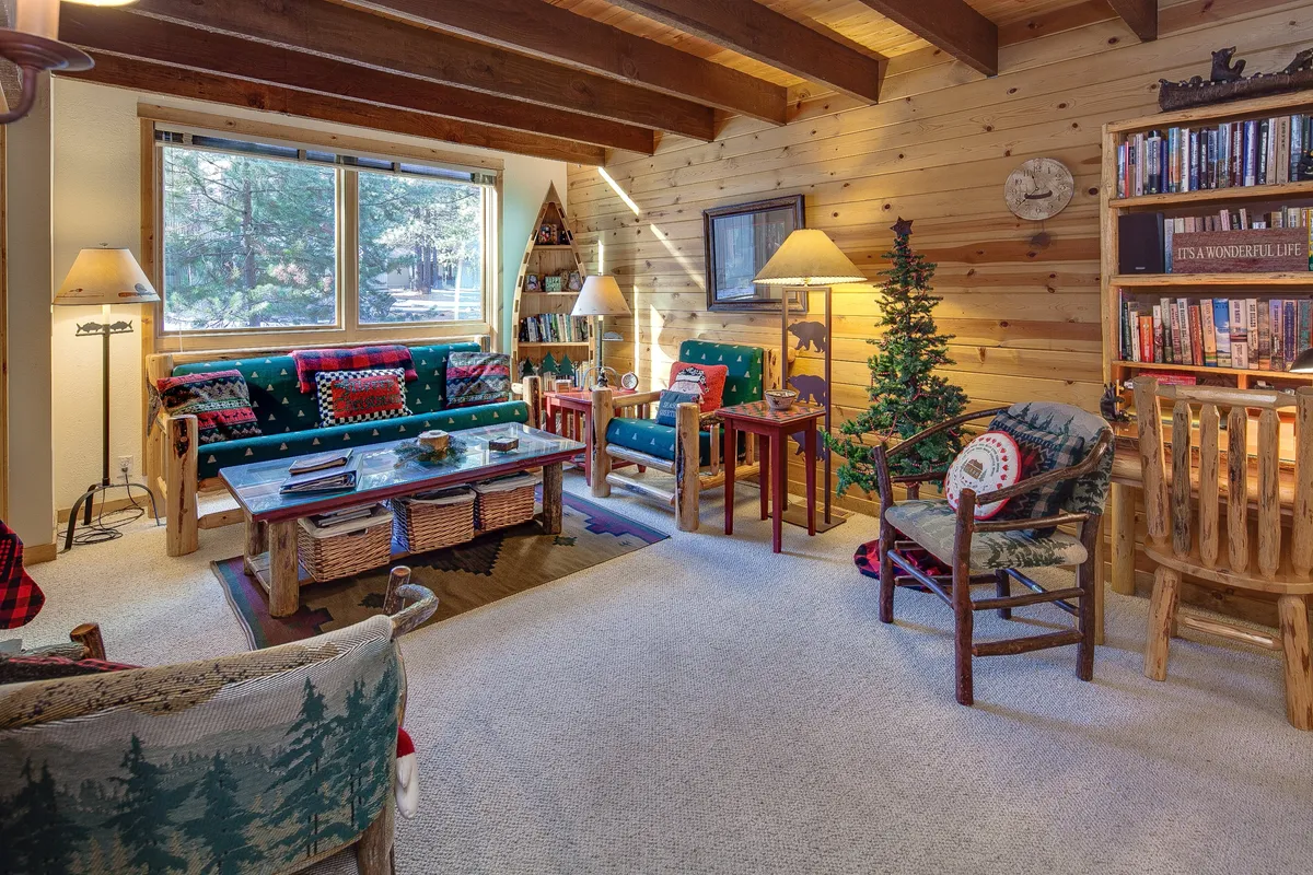 A sun-drenched living room with large windows, comfortable sofas, a bookcase filled with books, and a cozy coffee table arrangement. Decorative elements and a relaxed layout create an atmosphere perfect for unwinding or hosting gatherings.