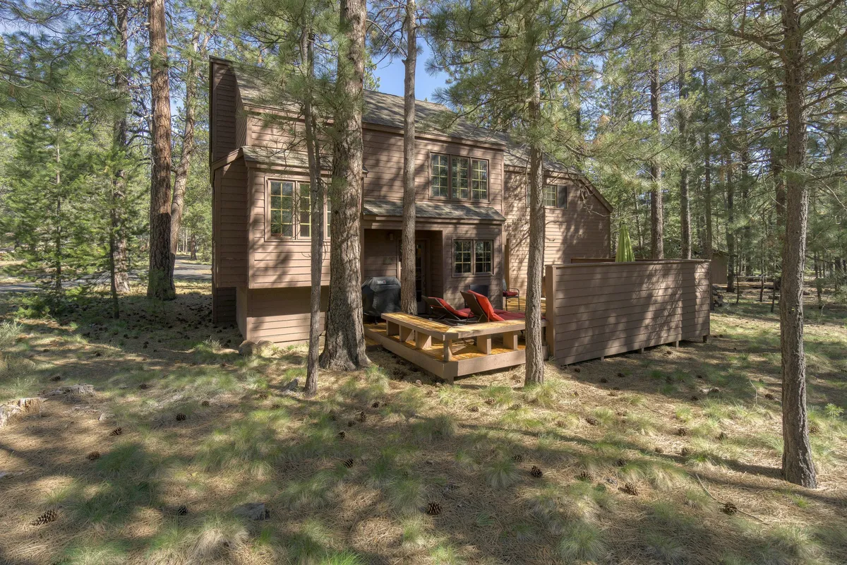 An inviting wooden deck surrounded by tall pine trees, featuring two red lounge chairs and a cozy atmosphere perfect for relaxing outdoors. The deck is spacious and provides a clear connection to nature, ideal for gathering with friends or stargazing at night.